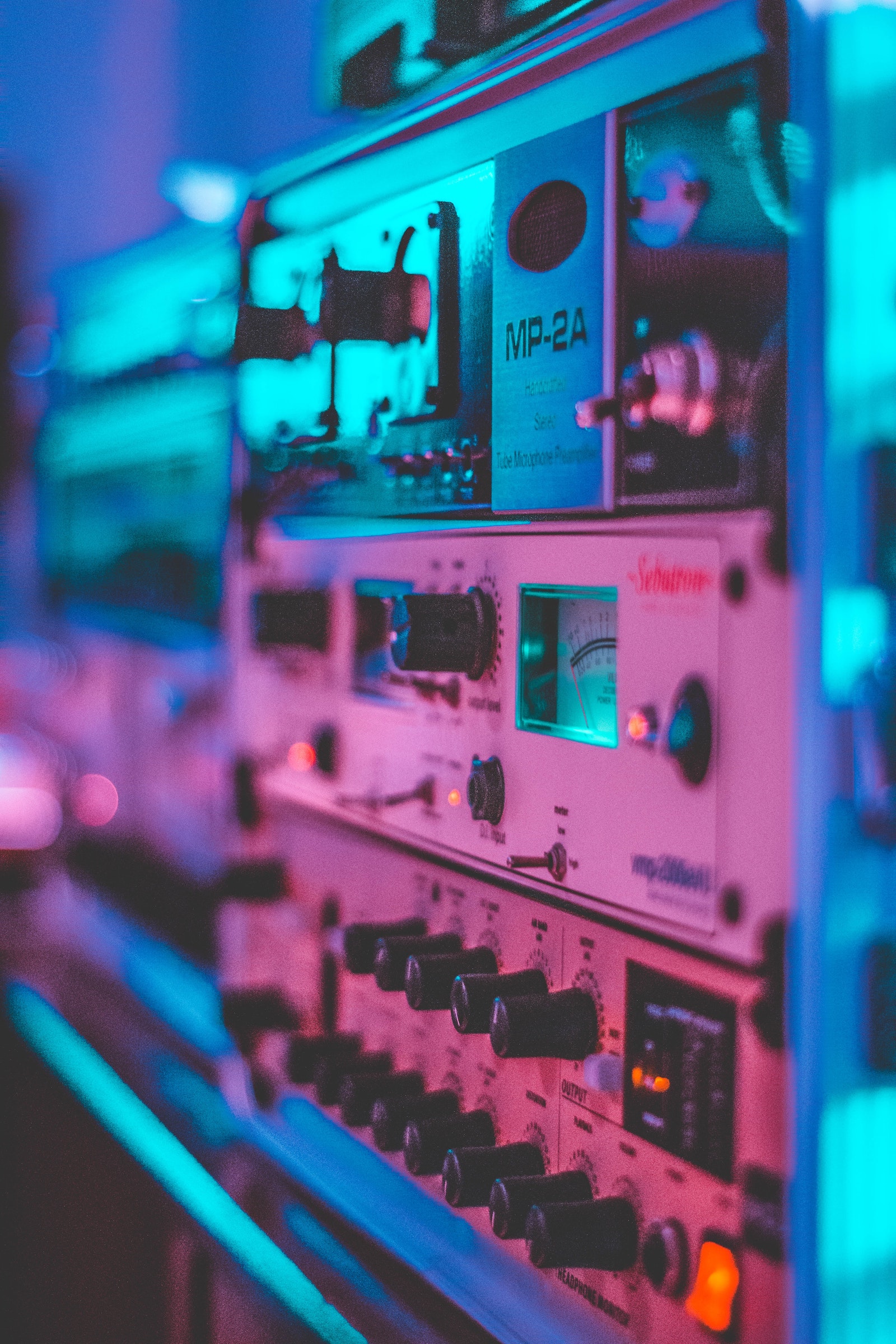 A collection of audio processing units in studio setting with a pink to blue neon light gradient.
